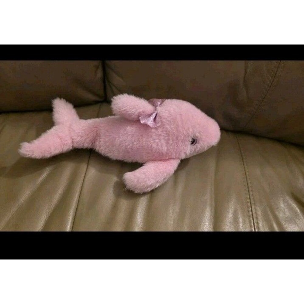 soft, light pink dolphin plush toy accented with a small, sparkly pink bow.